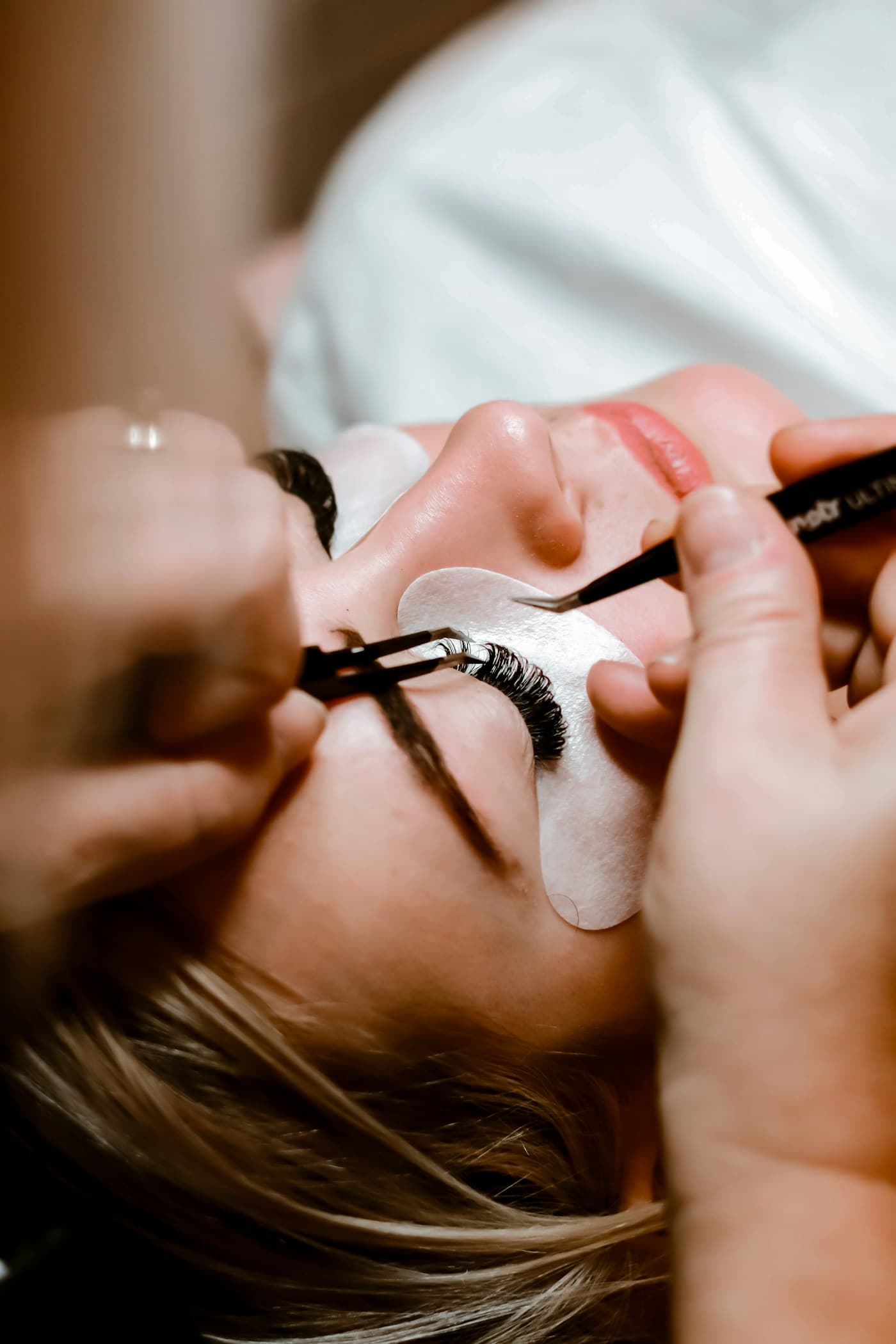 Lash technician applying lash extensions with tweezers