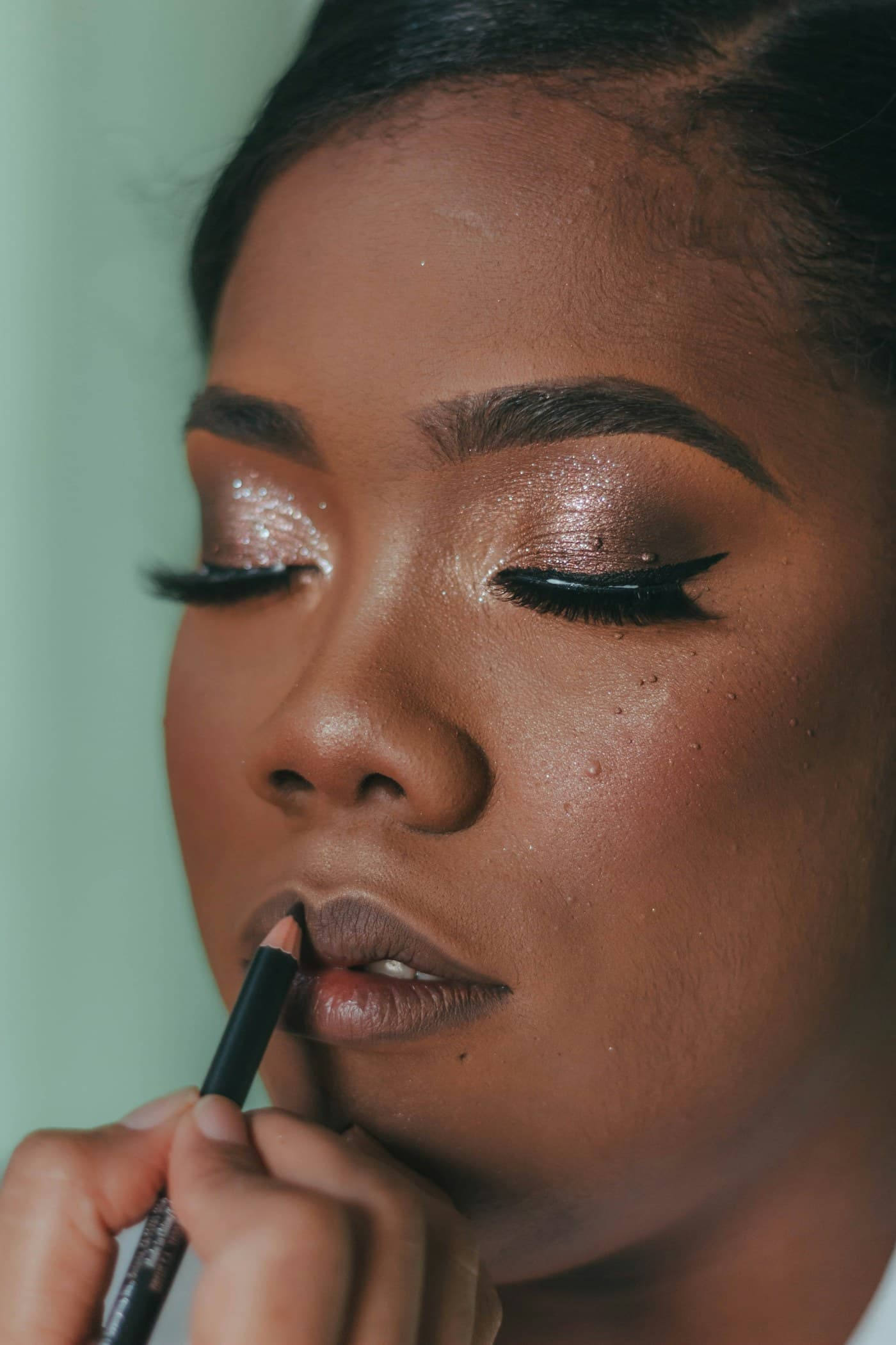 Close-up of lip liner being applied to a woman with shimmering eye makeup