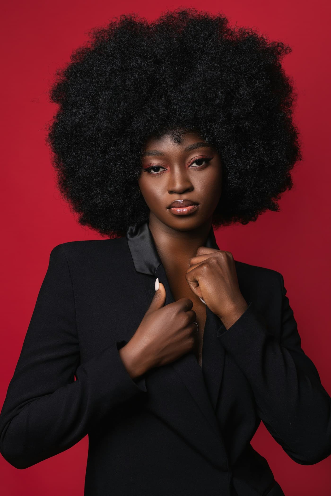 Woman with a full afro in a black blazer against red